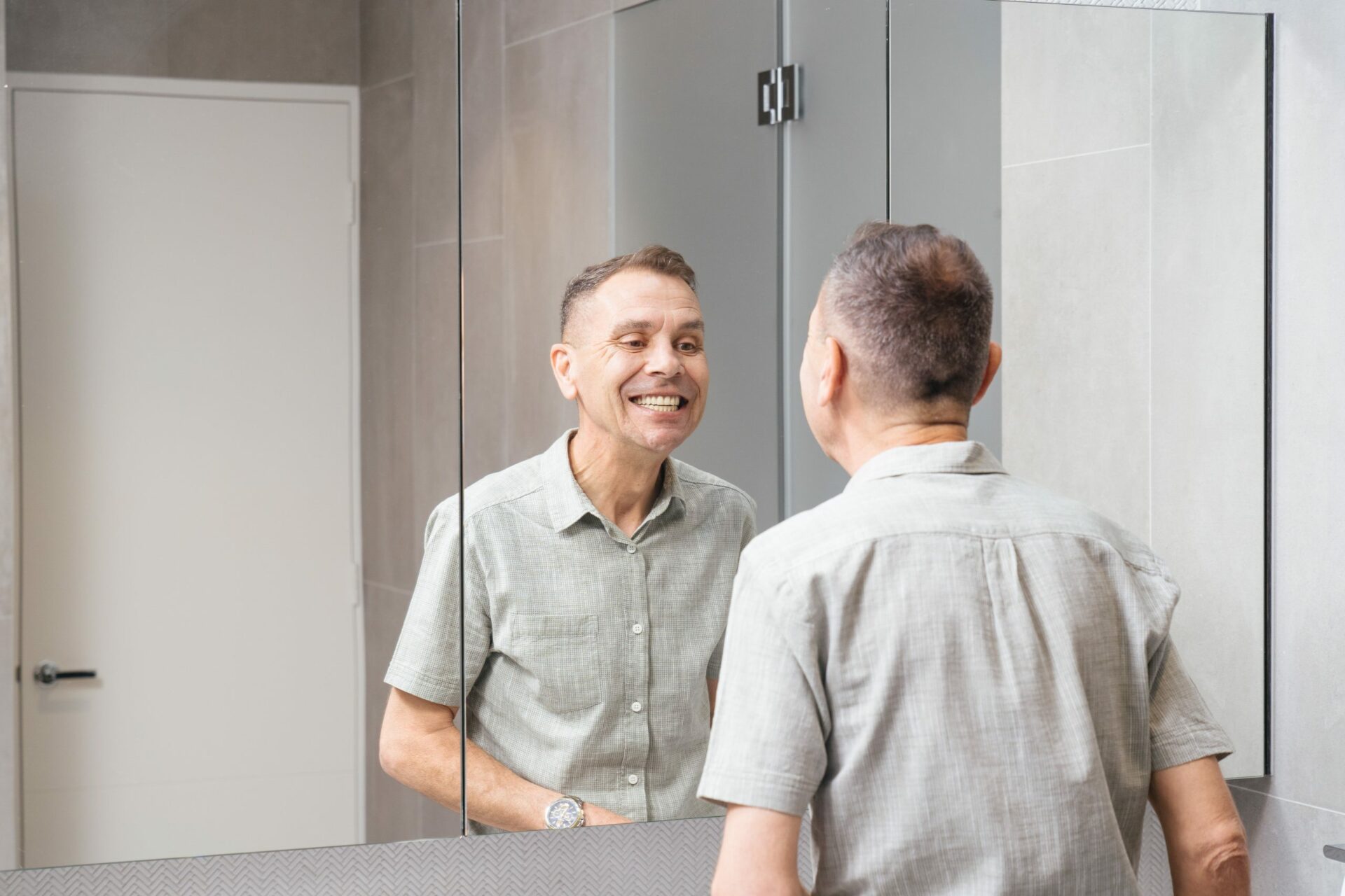 Man looking happily at his All on 4 Dental implants in the mirror.